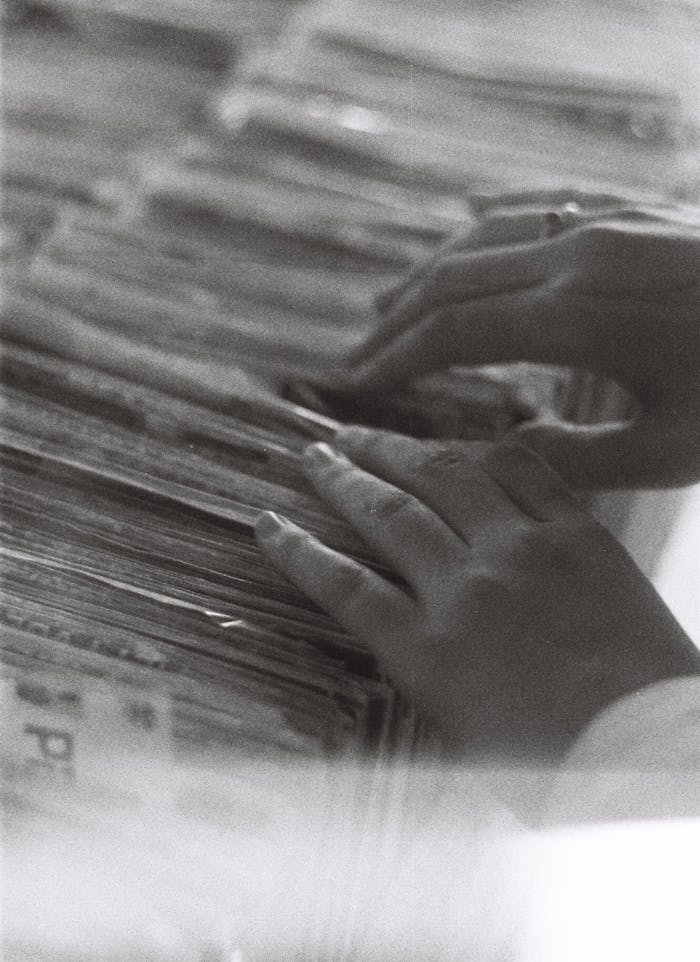 Hands browsing through a pile of vintage magazines in a retro black and white photo.