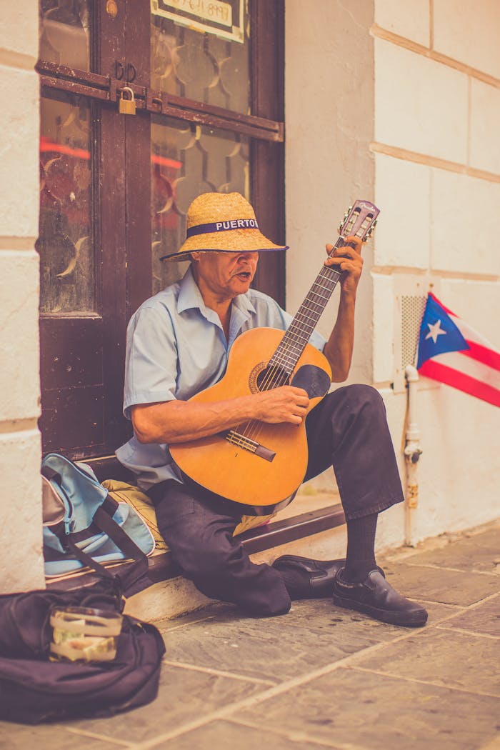 Old street musician playing guitar in San Juan with a Puerto Rican flag nearby.